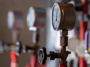 Druckanzeigen Das Bild zeigt drei Druckmessgeräte, die an Rohrleitungen angebracht sind. Im Vordergrund befindet sich ein Manometer mit einem schwarzen Ventilgriff. Im Hintergrund sind zwei weitere ähnliche Druckmesser zu erkennen, jedoch unscharf dargestellt.