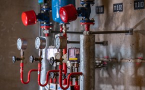 Mehrere mechanische Anzeigen im Heizkraftwerk Plauen Das Bild zeigt einen Ausschnitt eines Heizkraftwerkes. Sichtbar sind mehrere Druckanzeigen mit Zei-gern, Ventile und rote Rohrleitungen, die mit metallischen Zylindern und weiteren Komponenten ver-bunden sind.