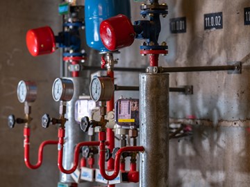 Mehrere mechanische Anzeigen im Heizkraftwerk Plauen Das Bild zeigt einen Ausschnitt eines Heizkraftwerkes. Sichtbar sind mehrere Druckanzeigen mit Zei-gern, Ventile und rote Rohrleitungen, die mit metallischen Zylindern und weiteren Komponenten ver-bunden sind.