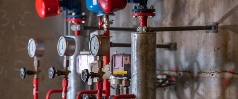 Mehrere mechanische Anzeigen im Heizkraftwerk Plauen Das Bild zeigt einen Ausschnitt eines Heizkraftwerkes. Sichtbar sind mehrere Druckanzeigen mit Zei-gern, Ventile und rote Rohrleitungen, die mit metallischen Zylindern und weiteren Komponenten ver-bunden sind.