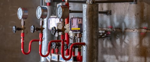 Mehrere mechanische Anzeigen im Heizkraftwerk Plauen Das Bild zeigt einen Ausschnitt eines Heizkraftwerkes. Sichtbar sind mehrere Druckanzeigen mit Zei-gern, Ventile und rote Rohrleitungen, die mit metallischen Zylindern und weiteren Komponenten ver-bunden sind.