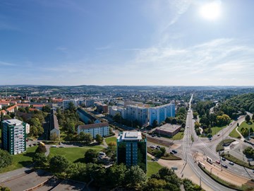 Panorama Plauen Wohnungsbau Das Bild zeigt eine Panoramaaufnahme einer Stadtlandschaft bei Tageslicht. Der Himmel ist klar und blau, die Sonne steht hoch oben rechts im Bild.