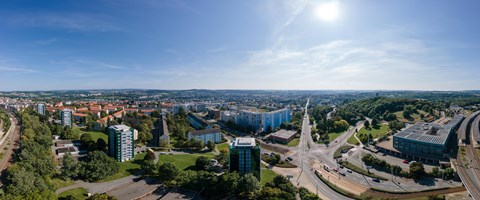 Panorama Plauen Wohnungsbau Das Bild zeigt eine Panoramaaufnahme einer Stadtlandschaft bei Tageslicht. Der Himmel ist klar und blau, die Sonne steht hoch oben rechts im Bild.
