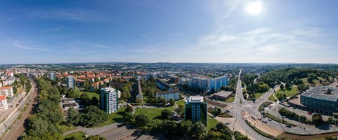 Panorama Plauen Wohnungsbau Das Bild zeigt eine Panoramaaufnahme einer Stadtlandschaft bei Tageslicht. Der Himmel ist klar und blau, die Sonne steht hoch oben rechts im Bild.