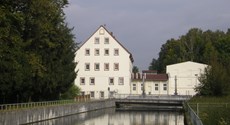 Blick über ein Wasserbecken auf die sich im Wasser spiegelnden Gebäude der Wasserkraftanlage Thierbach Blick über ein Wasserbecken auf die sich im Wasser spiegelnden Gebäude der Wasserkraftanlage Thierbach