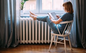 Frau mit Buch legt Beine auf einen Heizkörper Frau mit Buch legt Beine auf einen Heizkörper