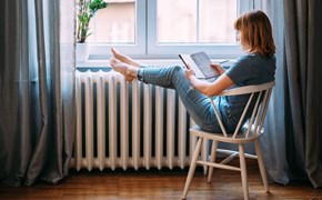 Frau mit Buch legt Beine auf einen Heizkörper Frau mit Buch legt Beine auf einen Heizkörper