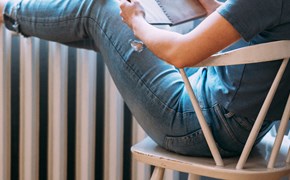 Frau mit Buch legt Beine auf einen Heizkörper Frau mit Buch legt Beine auf einen Heizkörper