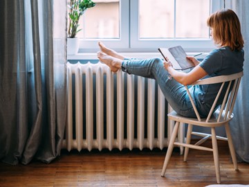 Frau mit Buch legt Beine auf einen Heizkörper Frau mit Buch legt Beine auf einen Heizkörper