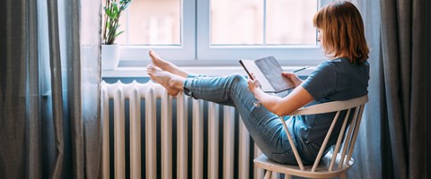 Frau mit Buch legt Beine auf einen Heizkörper Frau mit Buch legt Beine auf einen Heizkörper