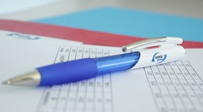 Kugelschreiber mit envia THERM-Logo liegt auf einem Tabellendokument Das Foto zeigt einen blau-weißen Kugelschreiber mit der Aufschrift „envia THERM“, der auf einem Blatt Papier liegt. Das Papier enthält Tabellen mit Zahlenwerten. Im Hintergrund sind weitere Blätter in Rot- und Blautönen zu sehen.