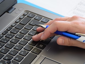 Nahaufnahme einer Hand mit Kugelschreiber auf der Tastatur Nahaufnahme einer Hand mit Kugelschreiber auf der Tastatur