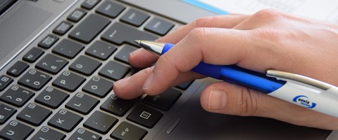 Nahaufnahme einer Hand mit Kugelschreiber auf der Tastatur Nahaufnahme einer Hand mit Kugelschreiber auf der Tastatur