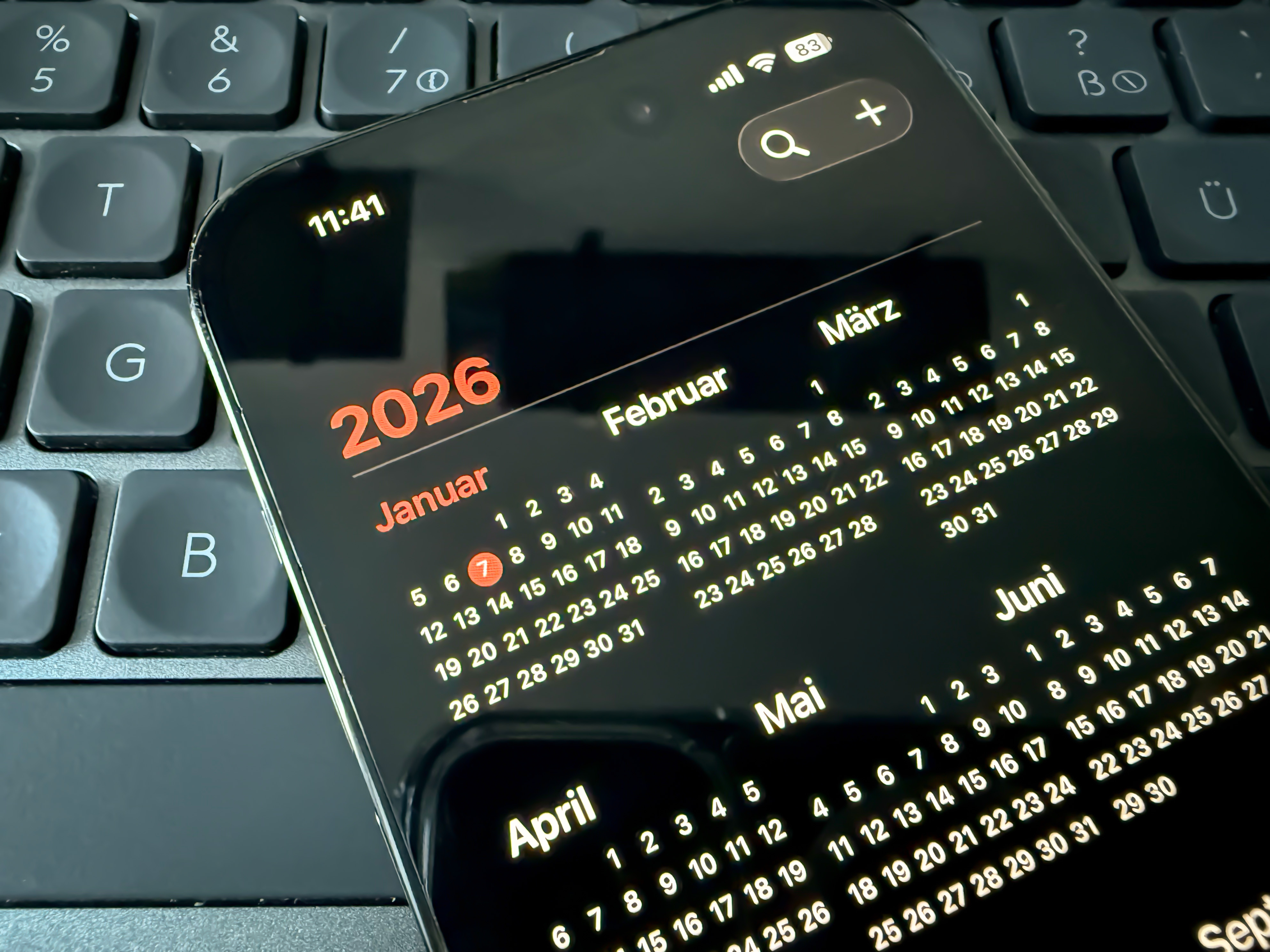 Ein Smartphone mit geöffneter Kalenderansicht für das Jahr 2026 liegt auf einer schwarzen Computertastatur. Auf dem Display sind die Monate des Jahres in kleiner Schrift zu sehen, der Januar ist hervorgehoben.