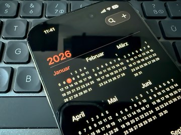 Unternehmensnachrichten Ein Smartphone mit geöffneter Kalenderansicht für das Jahr 2026 liegt auf einer schwarzen Computertastatur. Auf dem Display sind die Monate des Jahres in kleiner Schrift zu sehen, der Januar ist hervorgehoben.