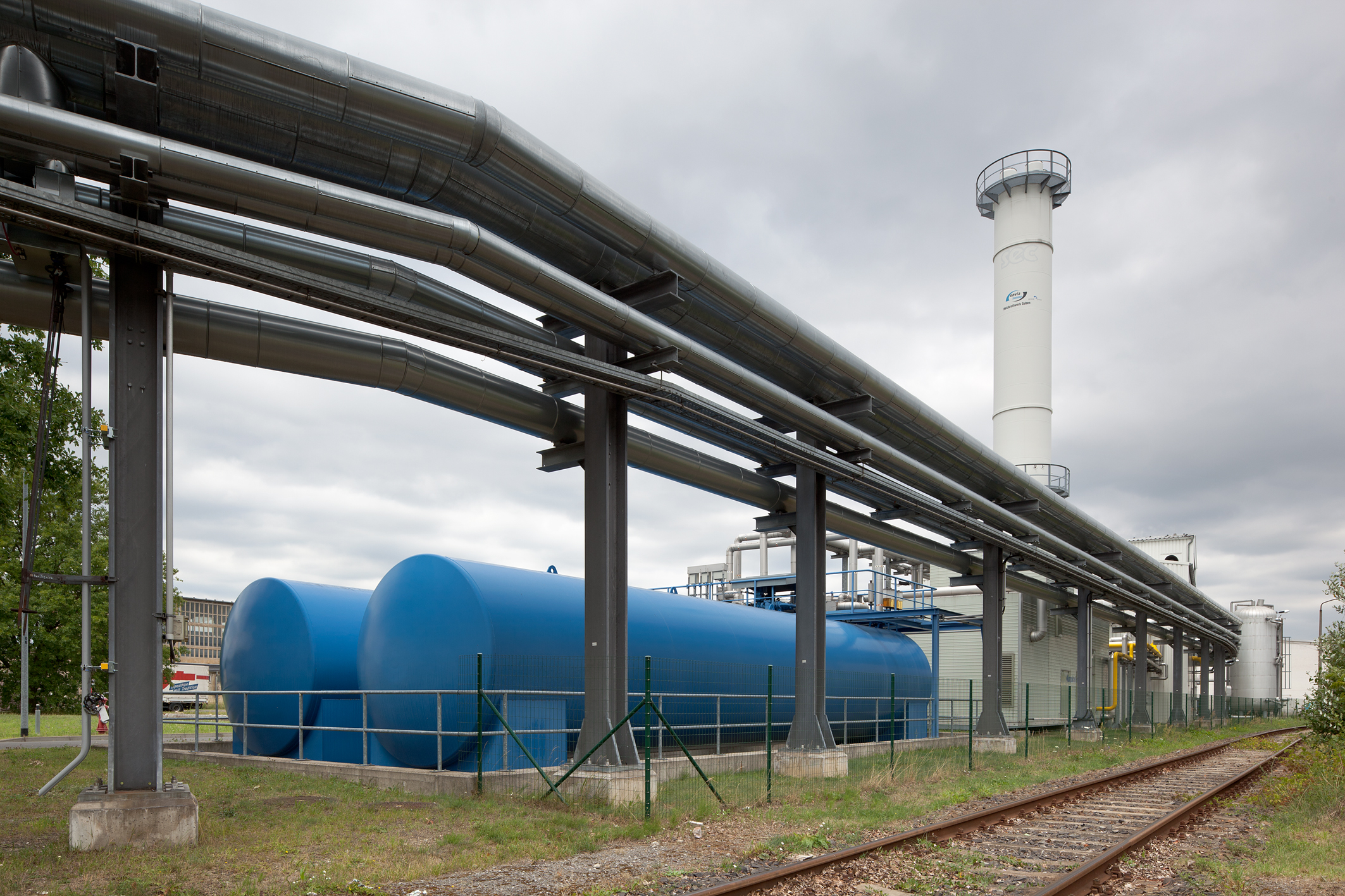 Außenaufnahme des Heizkraftwerks Guben, im Vordergrund ein Versorgungsrohrsystem und blaue Tanks 