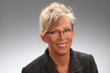 Ute Haupt Eine Person mit nach hinten gebundenen blonden Haaren ist zu sehen. Sie trägt eine Brille und ein dunkel gefärbtes Sakko.