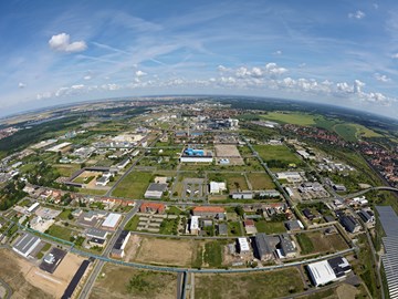 Luftbild Chemiepark Bitterfeld Das Bild ist eine Luftaufnahme, die eine Mischung aus städtischer und ländlicher Landschaft zeigt. Im Vordergrund befinden sich Gebäude, Straßen und grüne Flächen. Im Mittel- und Hintergrund erstreckt sich eine Stadt mit Wohnhäusern und Industrieanlagen.