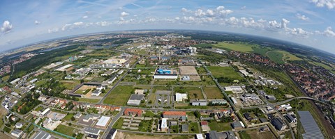 Luftbild Chemiepark Bitterfeld Das Bild ist eine Luftaufnahme, die eine Mischung aus städtischer und ländlicher Landschaft zeigt. Im Vordergrund befinden sich Gebäude, Straßen und grüne Flächen. Im Mittel- und Hintergrund erstreckt sich eine Stadt mit Wohnhäusern und Industrieanlagen.